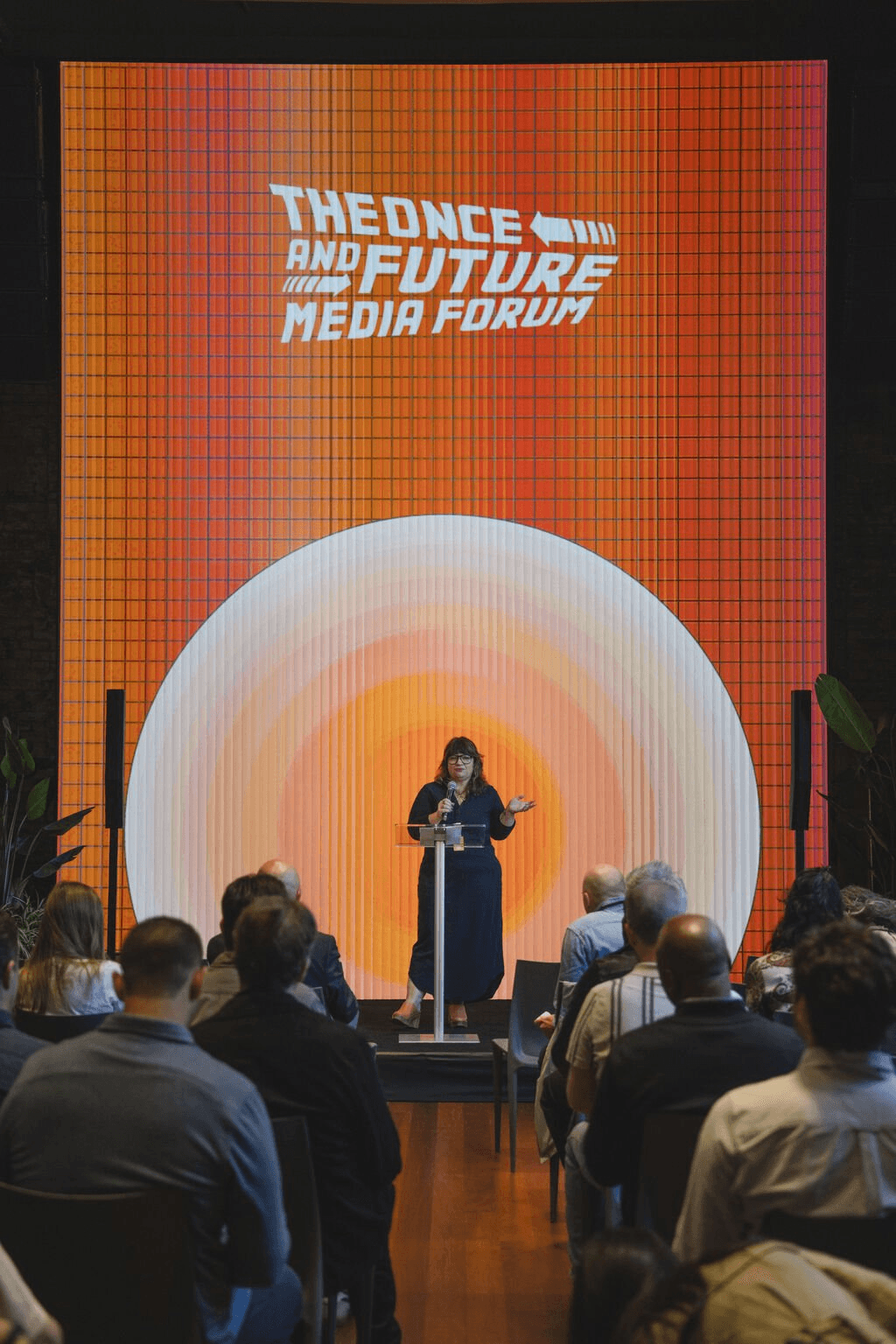 Warm orange LED wall with concentric rings behind a speaker at a Substack event